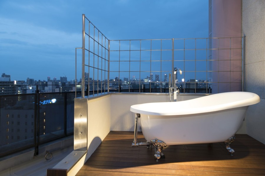 Clawfoot bathtub on a rooftop deck at Hotel Alps with the Osaka skyline at dusk