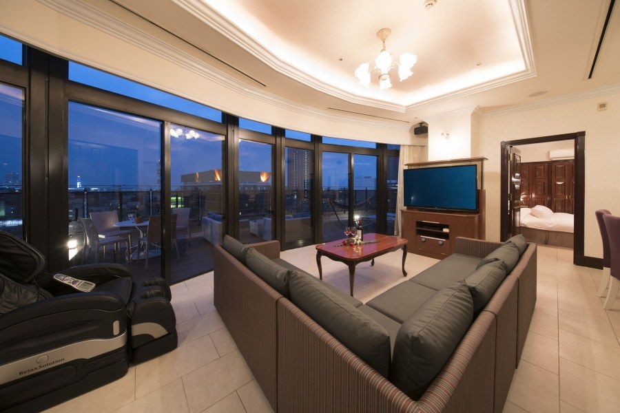 Suite living room at Hotel Alps with a large sectional sofa, a television and floor-to-ceiling windows over the city