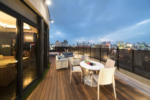 Rooftop terrace of a suite at Hotel Alps with a table, wicker sofas and the Namba skyline at dusk