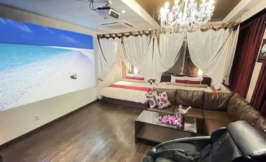 Suite at Hotel Balian Resort Namba Shinsaibashi with a wall-sized projected beach scene, a canopy bed, a corner sofa and a chandelier