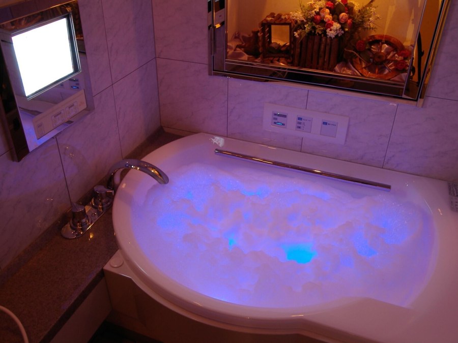 Jet bath filled with bubbles and lit in blue at Hotel Fine Garden Umeda, with a bathroom TV on the wall